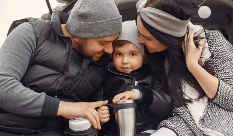 Family with cute little child. Father in a black jacket. People sitting on a trunk.